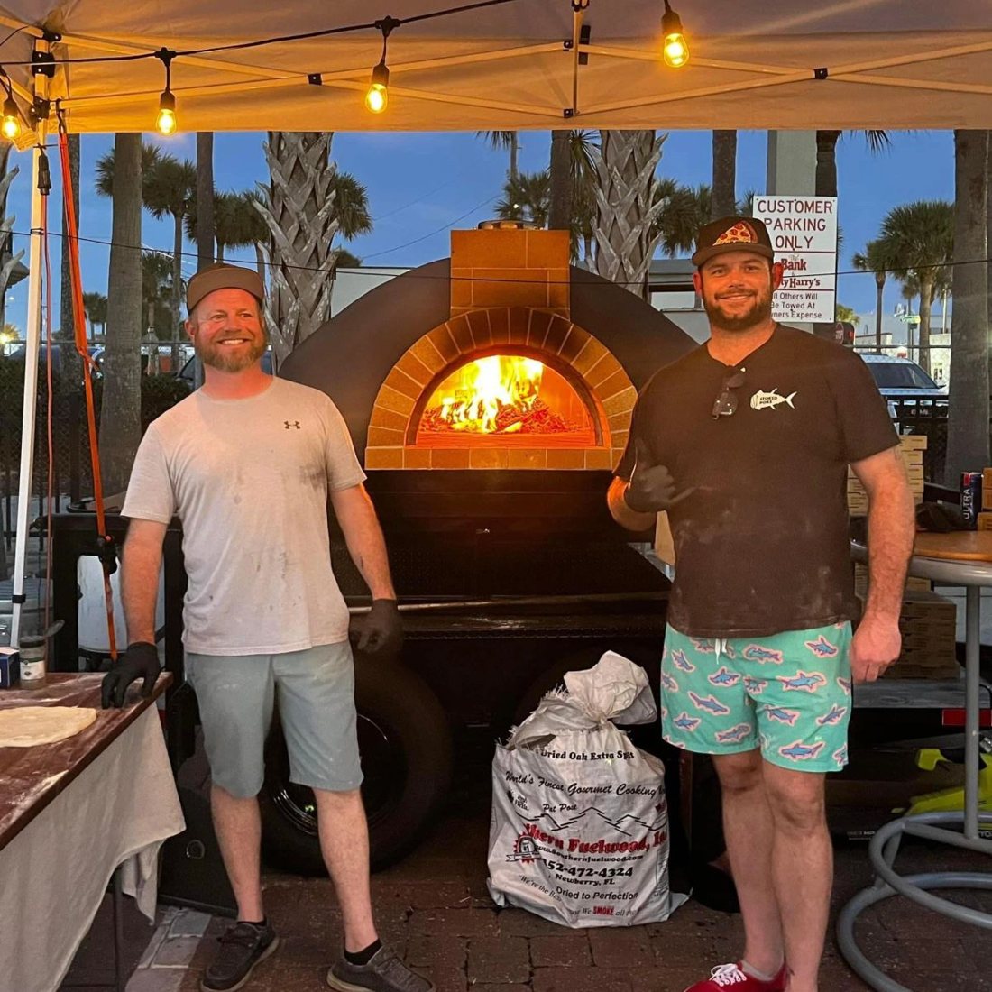 Ryan and Eric beside the trailer-mounted wood-fired oven at dusk